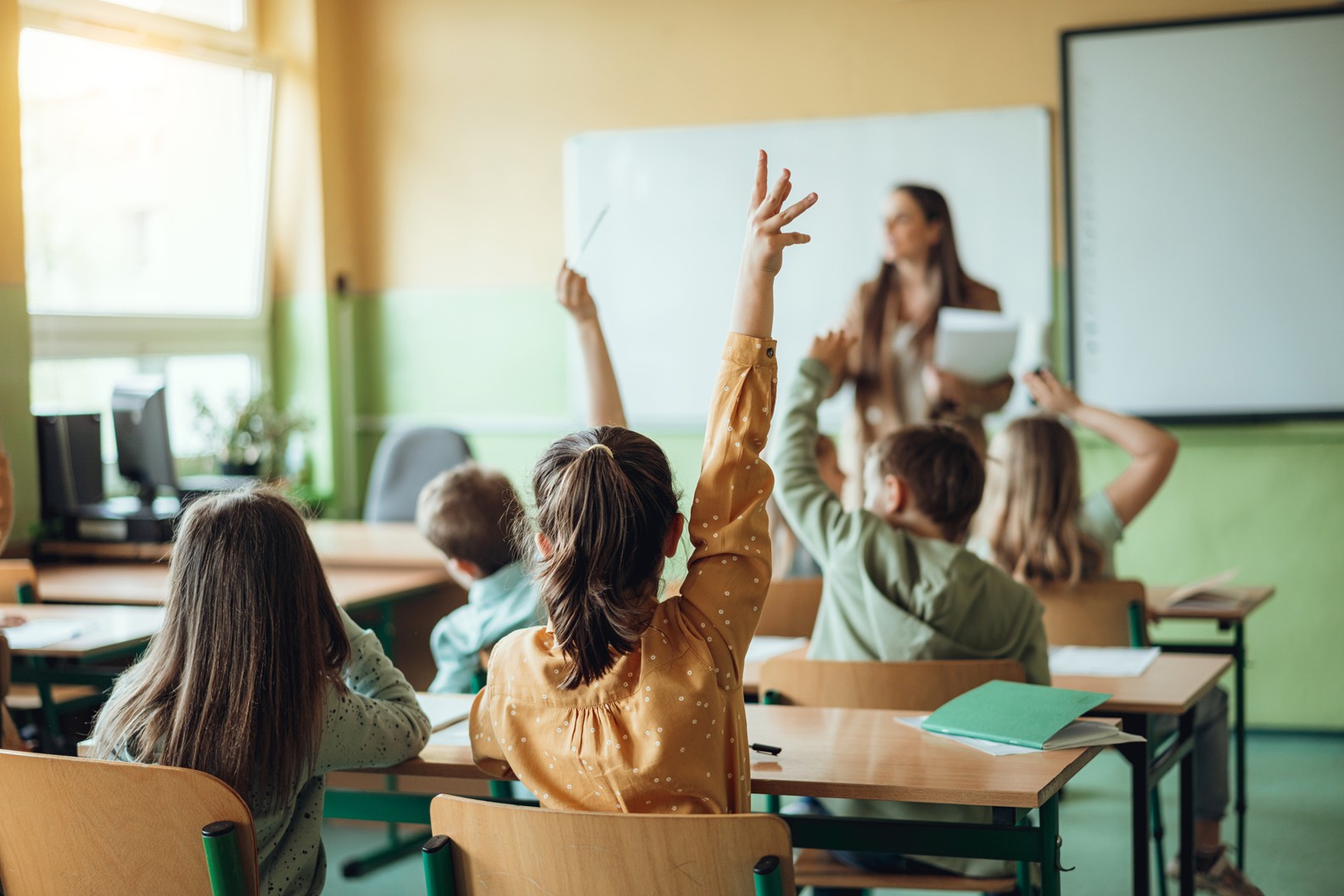 young students raising hands in a classroom